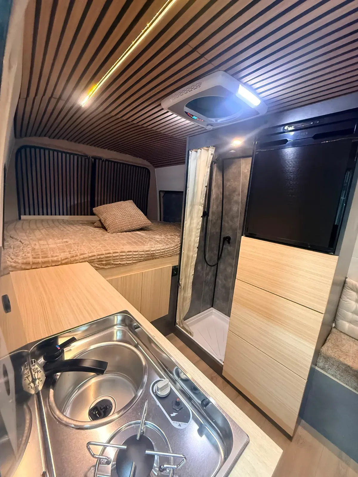 Interieur van omgebouwd busje met bed, keukenblok, spoelbak en douchecabine