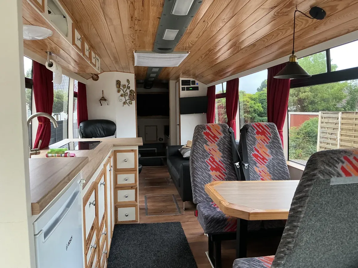 Ingerichte leefruimte van de omgebouwde touringcar met keukenblok, zithoek en eettafel.