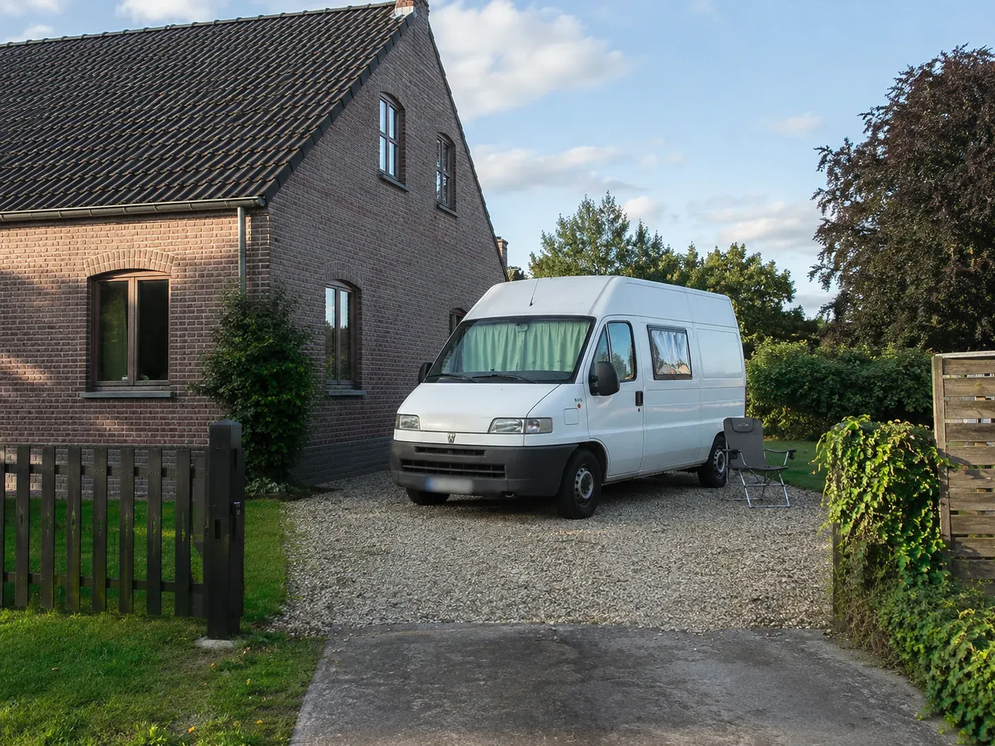 Witte van op grindoprit voor bakstenen huis met tuin en hek.