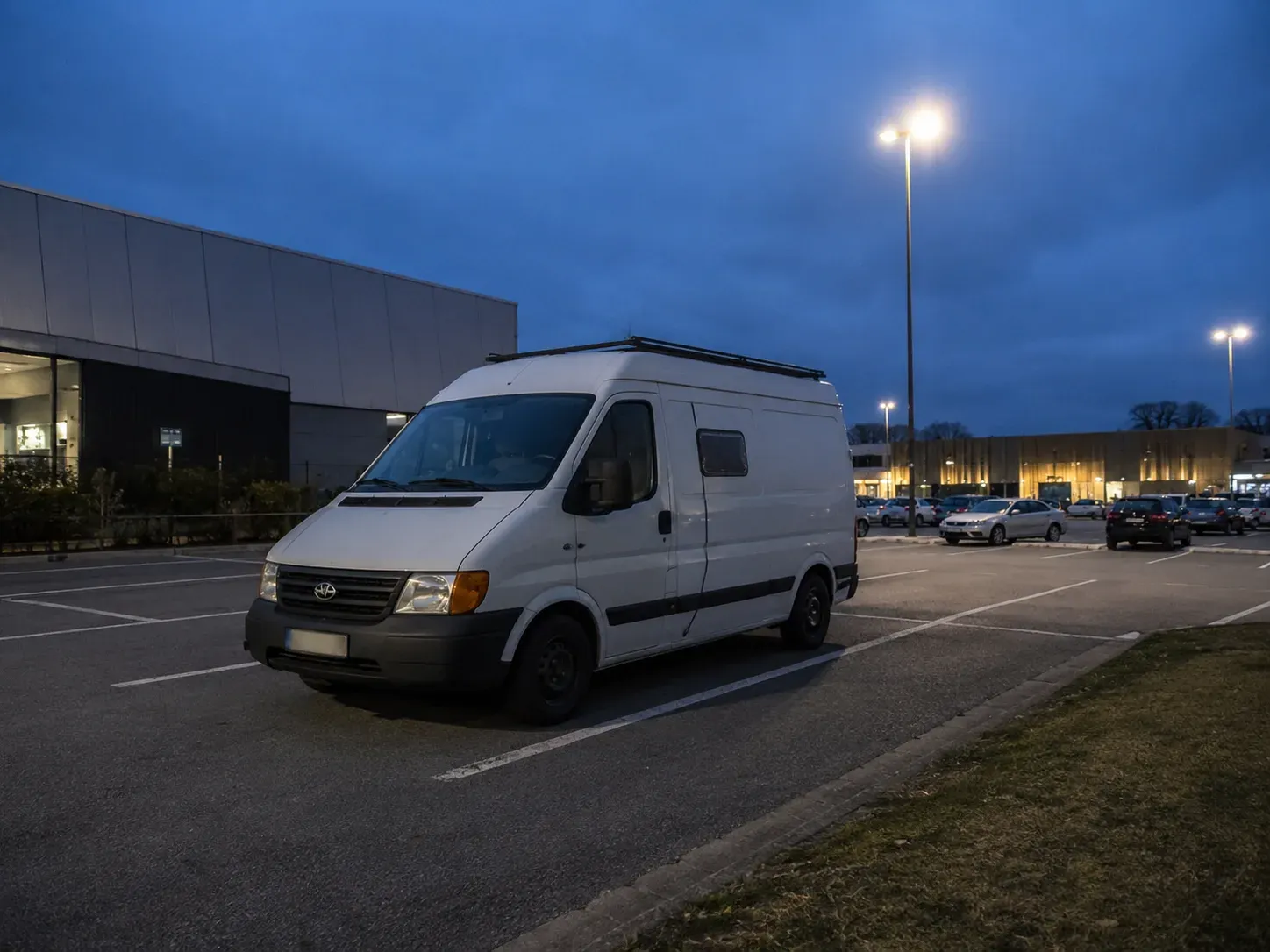 Witte van geparkeerd op een verlichte parking van een winkelcentrum bij avond.